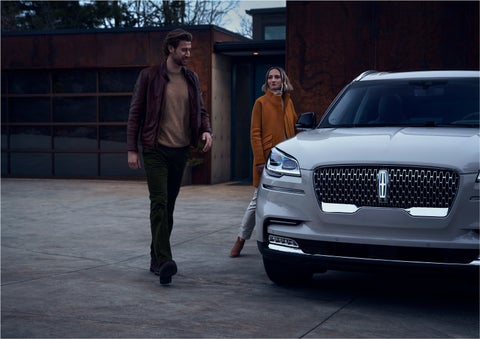 A man and a woman approaching a 2023 Lincoln Aviator® SUV, which illuminates certain lights when they are close | Star Lincoln in Southfield MI