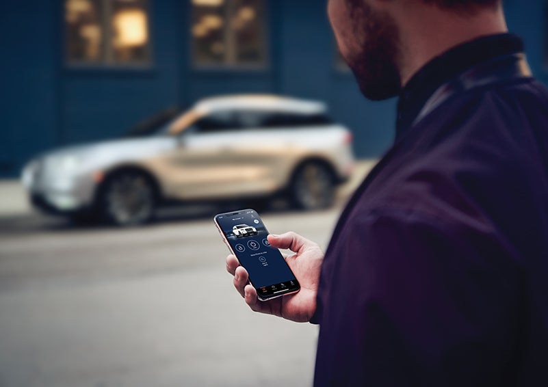 A person is shown interacting with a smartphone to connect to a Lincoln vehicle across the street. | Star Lincoln in Southfield MI