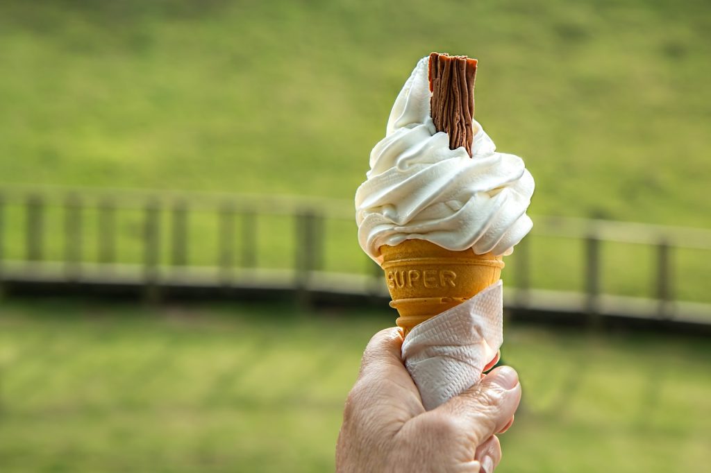 A hand holding a vanilla ice cream cone.