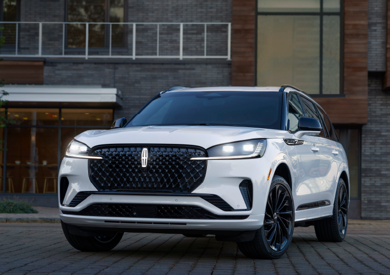 A white 2025 Lincoln Aviator® SUV is shown parked outside a modern building with gray brick and wood accents. | Star Lincoln in Southfield MI