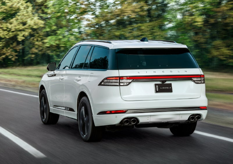 A white 2026 Lincoln Aviator® SUV is being driven away down a road lined with colorful trees. | Star Lincoln in Southfield MI