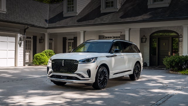 A white 2026 Lincoln Aviator® SUV is parked in the driveway of a luxury home. | Star Lincoln in Southfield MI