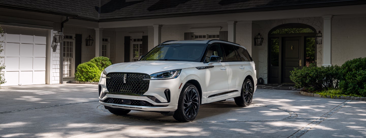 A white 2026 Lincoln Aviator® SUV is parked in the driveway of a luxury home. | Star Lincoln in Southfield MI