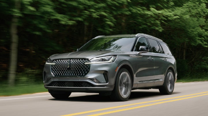 A 2027 Lincoln Aviator® SUV is being driven down a road lined with trees. | Star Lincoln in Southfield MI